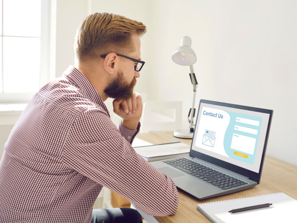 Homem analisando um formulário de contato em uma landing page no laptop, reforçando práticas essenciais de como fazer landing pages que aumentam as conversões.