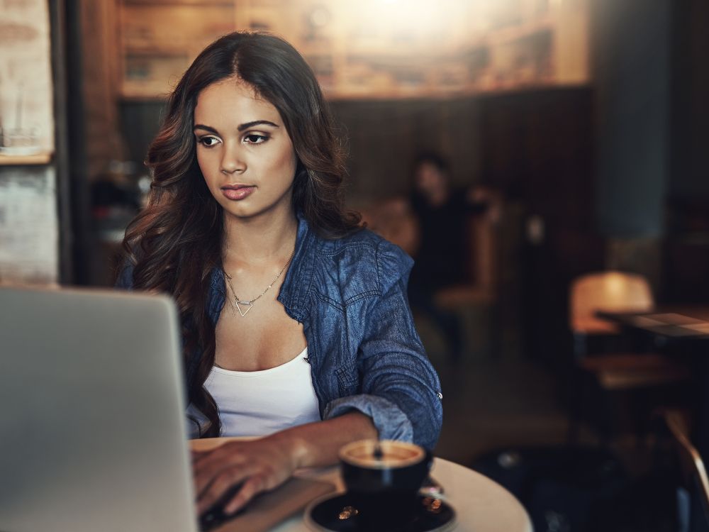 Mulher usando laptop em cafeteria, ilustrando o uso do WordPress por criadores de conteúdo e empreendedores digitais.