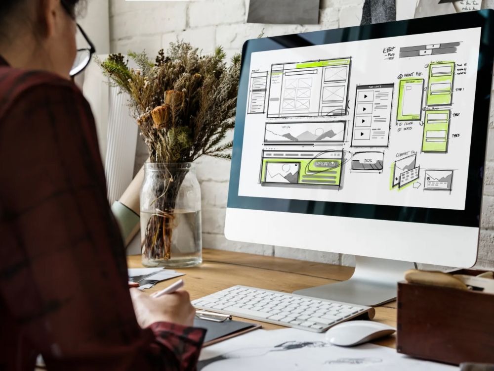 Designer projetando layout de site em computador, com estrutura de menus e rodapés para mostrar na prática o que é footer.